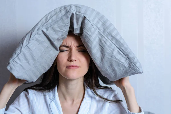 Retrato frontal de una mujer cansada y solitaria con una almohada en la cabeza sufriendo de insomnio. Vecinos ruidosos, migraña, dolor de cabeza —  Fotos de Stock