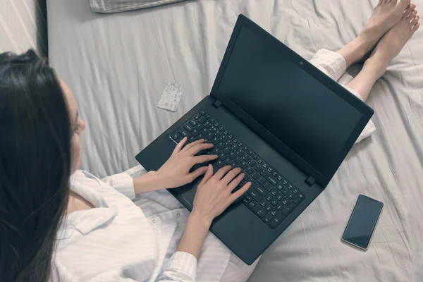 Female freelancer in her pajamas lying in bed and working on laptop, blogger, writer. cropped top view — Stock Photo, Image