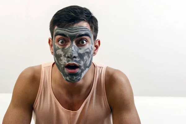 Retrato sorprendido de un hombre con una máscara de barro en su cara. cuidado de la piel. espacio de copia —  Fotos de Stock