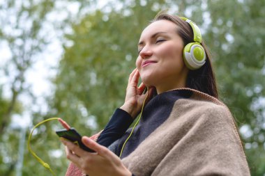Genç kadın parkta açık havada kulaklık ile akıllı telefon dinleme müzik. Alt görünümü
