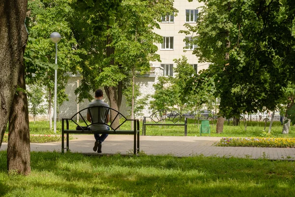 Un uomo seduto su una panchina che legge un libro in un parco verde all'aria aperta. vista posteriore — Foto Stock
