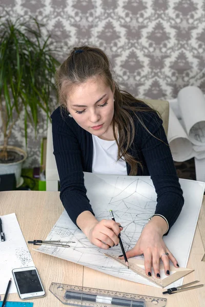 Portrait of a concentrated young student at the table is engaged in drawing architectural design, drawing, sketch, geometry, model