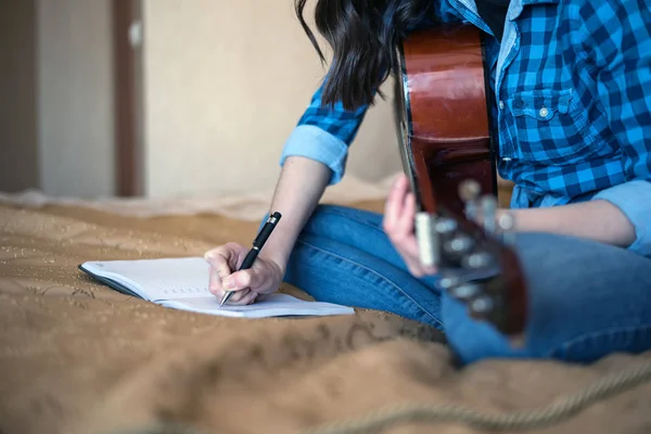 Περικομμένη εικόνα Γυναικεία χέρια που γράφει σε ένα σημειωματάριο με μια ακουστική κιθάρα — Φωτογραφία Αρχείου