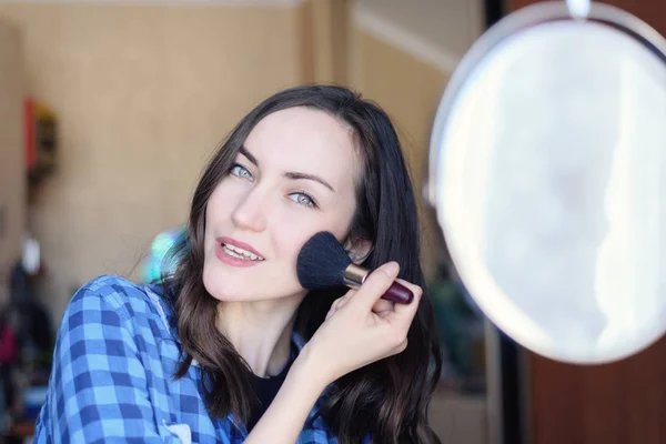 Junge Brünette korrigiert Make-up am runden Spiegel im Schlafzimmer — Stockfoto