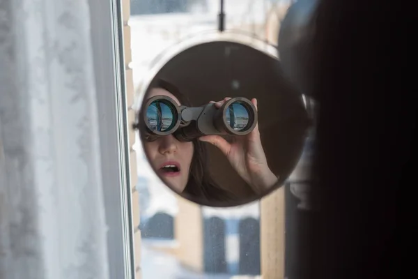 Portret zaskoczony brunetka z lornetki, patrząc przez okno, szpieguje sąsiadów — Zdjęcie stockowe