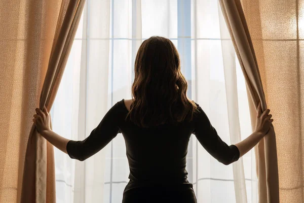 Молодая женщина открывает занавески у панорамного окна — стоковое фото