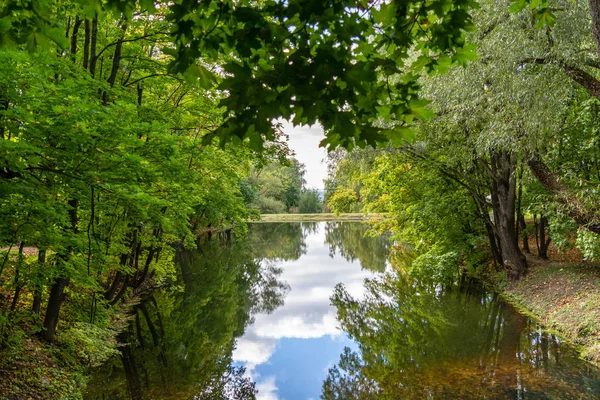 Sztuczne jezioro w zielonym parku liściastych z lustrzaną powierzchnią wody — Zdjęcie stockowe