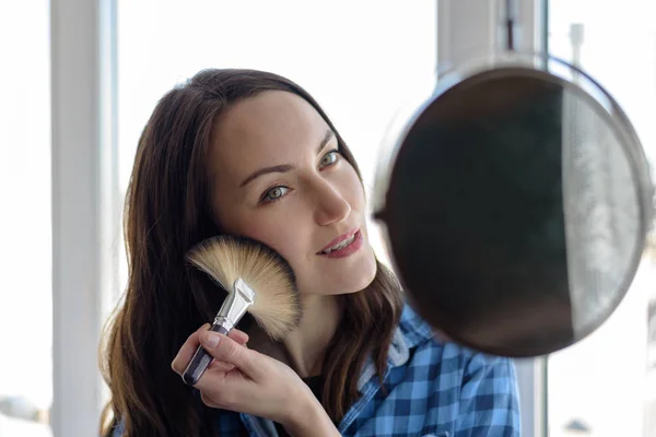 Gelukkige vrouw met cosmetische penseel make-up ronde spiegel wordt toegepast op de huidtoon Stockfoto