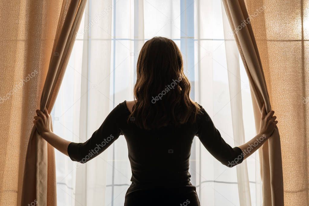 A young woman opens the curtains at the panoramic window