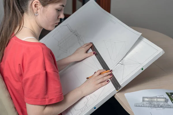 Vista lateral de uma jovem com uma placa gráfica desenha um esboço com uma régua e um lápis — Fotografia de Stock