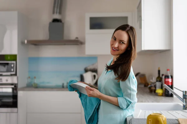 Retrato general de una joven en el interior de una cocina luminosa con una toalla y un plato en las manos. la vida real —  Fotos de Stock