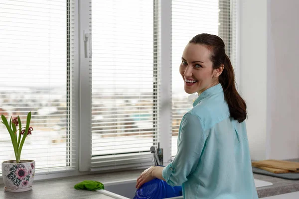 Retrato de niña sonriente lavando platos en la cocina frente a la ventana con persianas — Foto de Stock