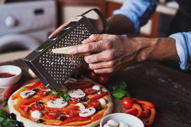 Erkeklerin elleri mantarlı, zeytinli ve vişneli hazır olmayan pizzalar için parmesan renginde.