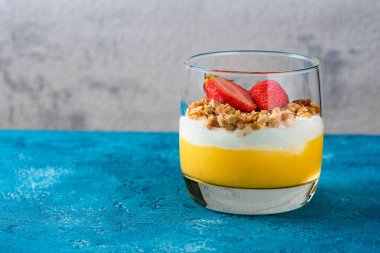 Bir bardak mangolu ve çilekli tatlı müsli ve kremalı veya turkuaz arka planda fotokopi alanlı ricotta.