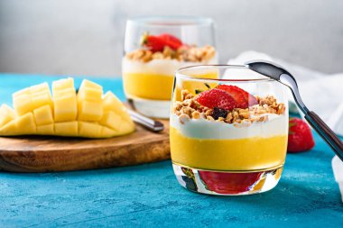 Meyveli bir tatlı ve bir kaşık mango, çilek, granola ve ricotta ile yakın plan.