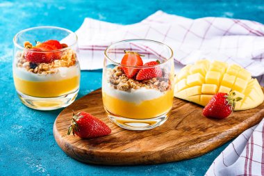 iki bardak mangolu ve çilekli tatlı müsli ve kremalı veya turkuaz arka planda tatlı kaşıklı ricotta