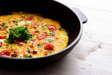 Makro, beyaz arka planda dökme demir bir tavada domatesli ve yeşillikli omleti kapat.