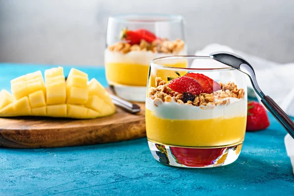 Крупный план стакана с фруктовым десертом и ложкой манго, клубники, мюсли и рикотты — стоковое фото