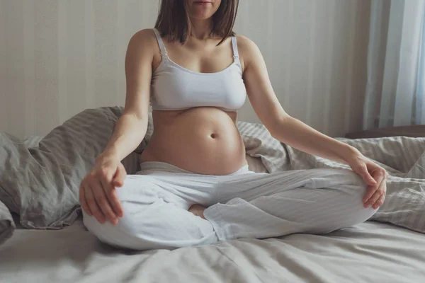 Donna incinta seduta sul letto con le mani in giro — Foto Stock