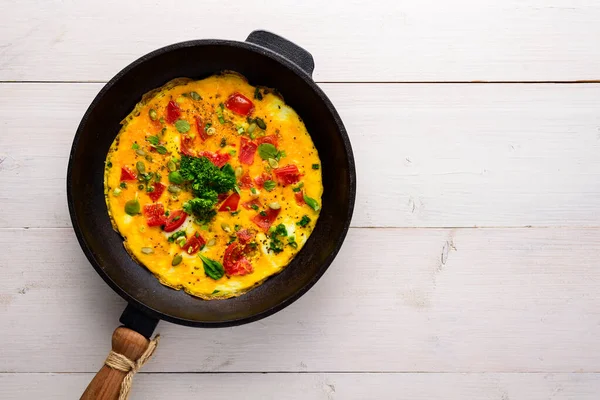 Ovos mexidos com tomates em uma antiga panela de ferro fundido em um fundo de madeira branca com um espaço de cópia — Fotografia de Stock