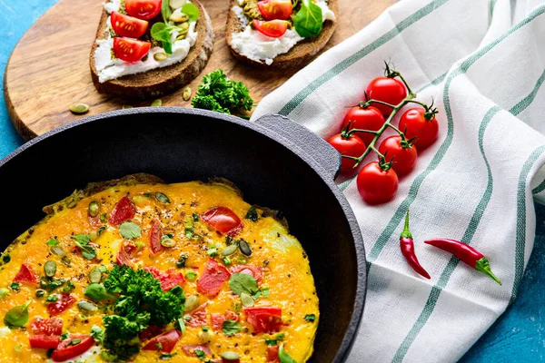 Café da manhã saudável em uma panela de ferro fundido. Ovos mexidos com verduras e tomates, sanduíches com creme de queijo, pesto e tomate cereja — Fotografia de Stock