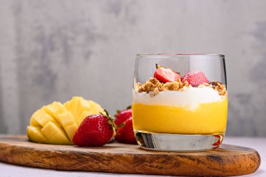 Meyveli bir tatlı ve mango, çilek, granola ve ricotta karışımı beyaz arka planda tahtadan yapılmış bir kaşıkla yakın plan.