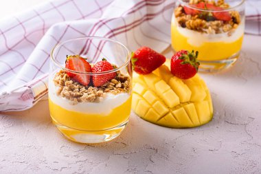 Krem peynirli tatlı, mango, granola ve pembe arka planda çilek.