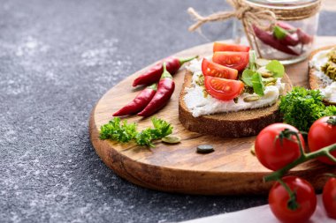 Süzme peynirli tost, pesto sosu, acı biber ve kiraz domatesli ahşap tahta üzerinde siyah arka plan