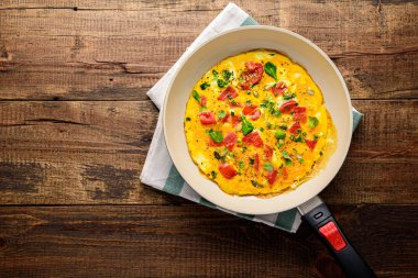 Domatesli omlet ve kahverengi ahşap arka planda kızartma tavasında ıspanak.