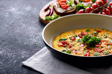 Domatesli çırpılmış yumurta, ıspanak ve kabak tohumları kızarmış tavada kızarmış ekmek, pesto sosu, kırmızı biber ve siyah arka planda vişne domatesleri.