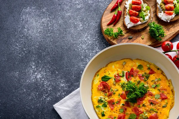 Zdravá snídaně omelety s cherry rajčaty a špenátem na pánvi a tousty s tvarohem, pesto omáčkou a cherry rajčaty na černém pozadí — Stock fotografie