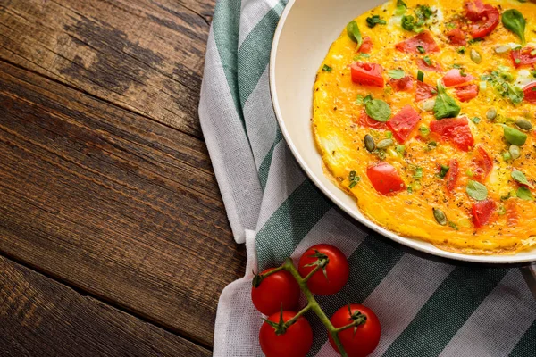 Imagem da colheita de omelete com tomate cereja e espinafre na frigideira no guardanapo de pano no fundo de madeira marrom — Fotografia de Stock