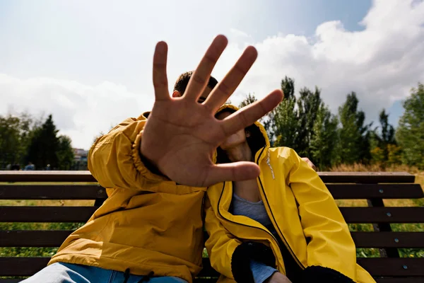 Joven pareja en chaquetas amarillas sentado en el banco en el otoño Parque cubre sus rostros con la mano —  Fotos de Stock