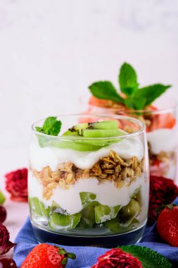 Kivi, çilek, krema, granola ve açık pembe arkaplanda naneli tatlının dikey görüntüsü