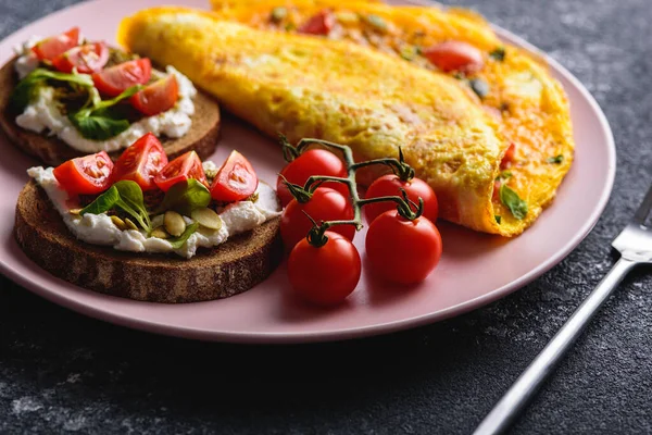 Śniadanie z omletem i chleb zbożowy z serem śmietankowym, pesto i pomidorami wiśniowymi na różowym talerzu z bliska — Zdjęcie stockowe