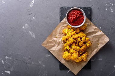 Kraft kağıdında domates soslu karnabahar. Gri arkaplan ve kopyalama alanı var.