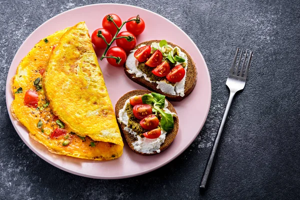 Close up saudável Pequeno-almoço de omelete de ovo, torrada integral com queijo creme, pesto e tomate cereja em uma placa rosa, em um fundo de pedra preta com um espaço de cópia . — Fotografia de Stock