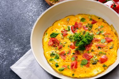 Domatesli omlet, yeşillik, ıspanak ve kabak tohumları siyah arka planda kızartma tavasında.