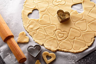 top view of cookie dough with cut out shapes in the form of heart on white parchment paper