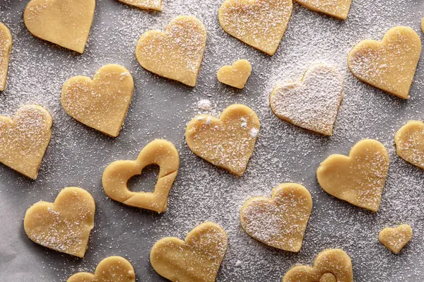 Biscuits non cuits en forme de cœur sur du papier blanc parchemin saupoudré de sucre en poudre — Photo