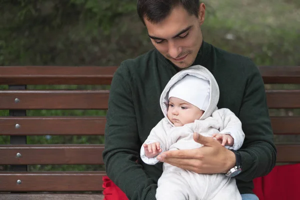 Bekar baba, parkta kucağında bebekle bankta oturur. — Stok fotoğraf