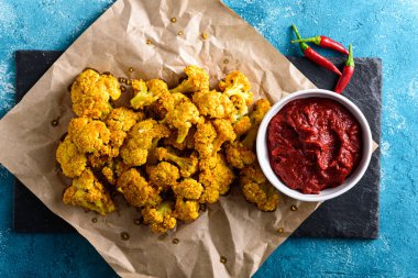 Kırmızı soslu vejetaryen karnabahar manzarası ve mavi arka planda biber.