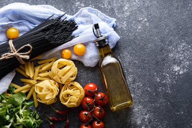 Siyah arka planda siyah makarna, fettucine, domates, mısır salatası ve bir şişe zeytinyağı, İtalyan yemeği.