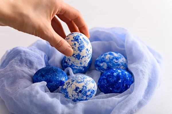 Hand lays Easter egg in the color of the year classic blue with gradient effect in fabric nest on white background — 스톡 사진
