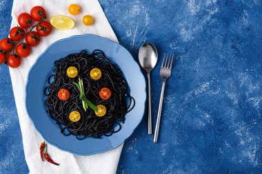 vejetaryen yemek siyah makarna mürekkepbalığı mürekkebi ile sarı ve kırmızı domatesler mavi arka planda çatal ve kaşıkla mavi tabakta