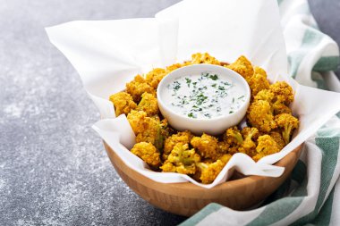 Ahşap kasede kızartılmış karnabahar ve gri arka planda sos.