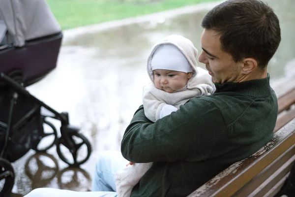 Beyaz adam yeşil ceketli baba bankta oturmuş bebeğine sarılıyor. — Stok fotoğraf