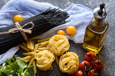 Pastel eflatun peçete, fetuçin, domates, mısır salatası, gri arka planda zeytinyağı.