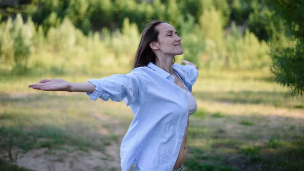 Authentic portrait of a smiling woman in blue shirt with her arms spread and eyes closed in nature — Stock Photo, Image