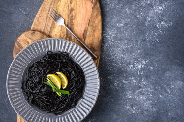 Üst görünüm, mürekkep balığı mürekkebi ve limon dilimleri olan siyah makarna. Gri arkaplanda tahta tabakta gri bir yaprak.